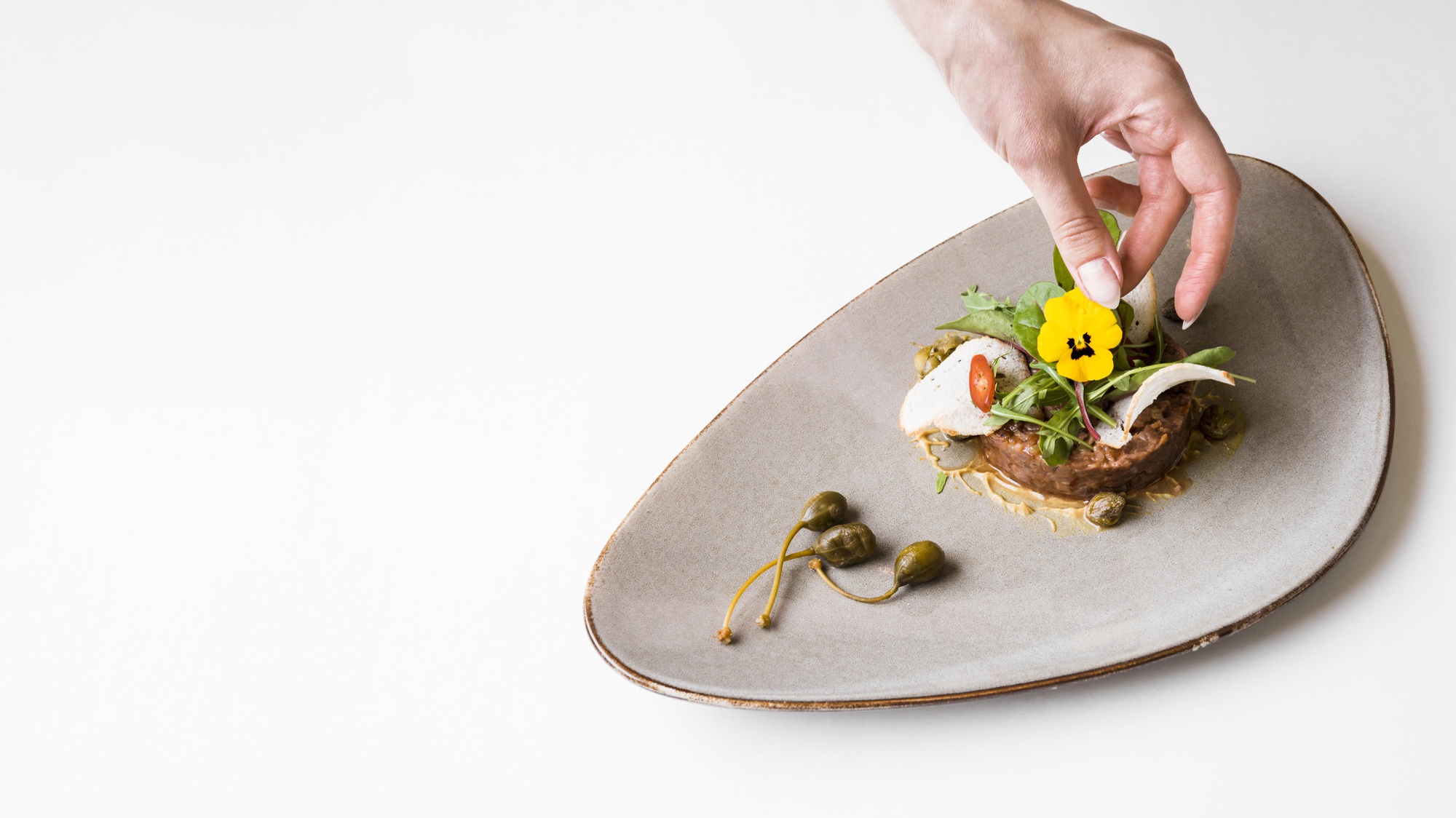 Hand finishing a plated gourmet dish on a wooden table
